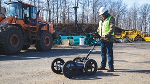 GPR operator using a ground penetrating radar system with GPS receiver pole attached for use on a construction site.